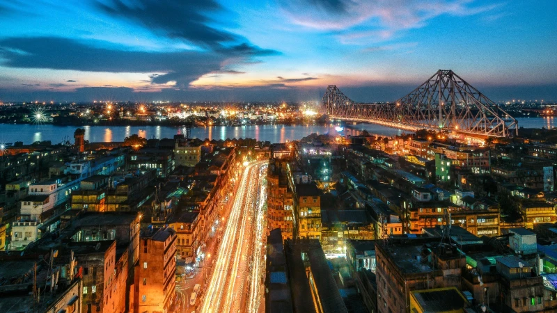 Aerial view of Kolkata city at dusk featuring the iconic Howrah Bridge and vibrant city lights