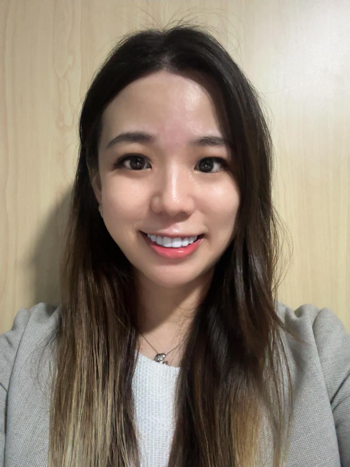 Ke Min Tan, professional at Vehere, wearing a light gray blazer over a white top, standing against a wooden background.